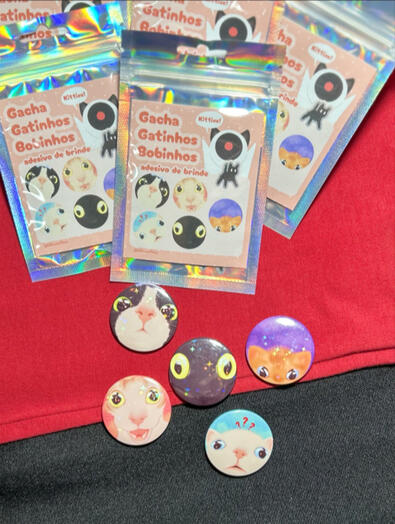 Gacha "Gatinhos Bobinhos" contendo um botton sortido de gato e um adesivo